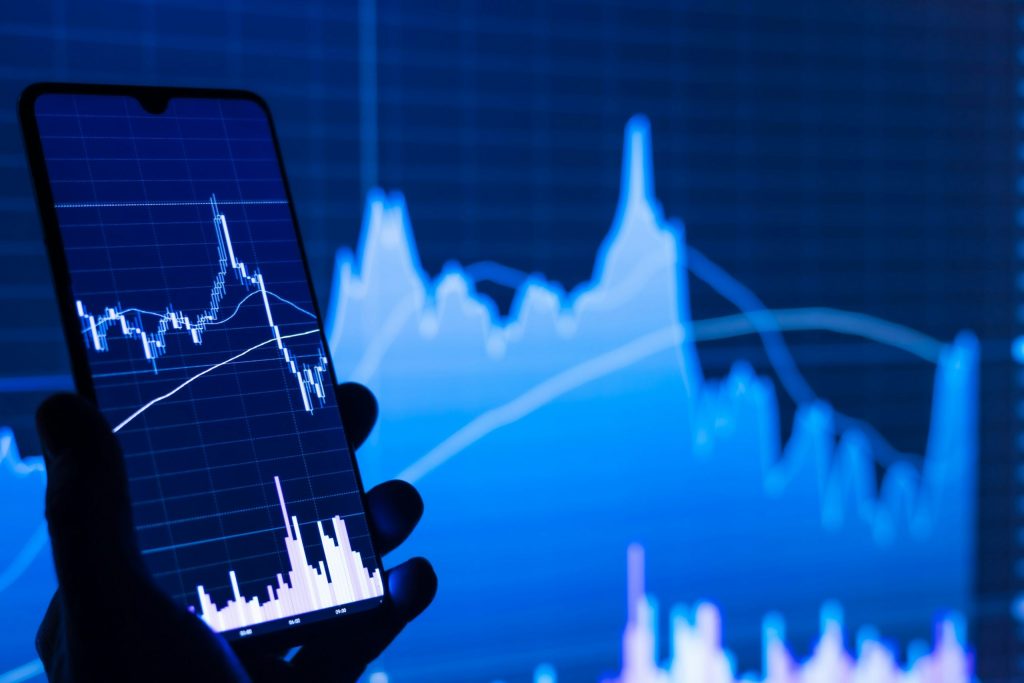 A hand in shadow holding a phone that is displaying a drop in a financial stock.