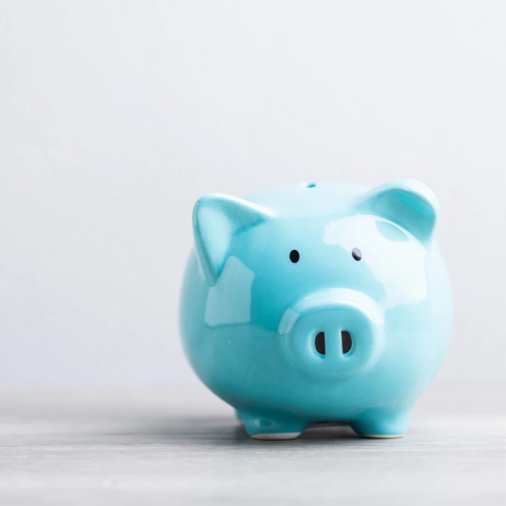 A blue piggy bank sits on a wooden table against a grey background, with ample copy space for text. The image symbolizes savings, financial planning, and responsible money management.